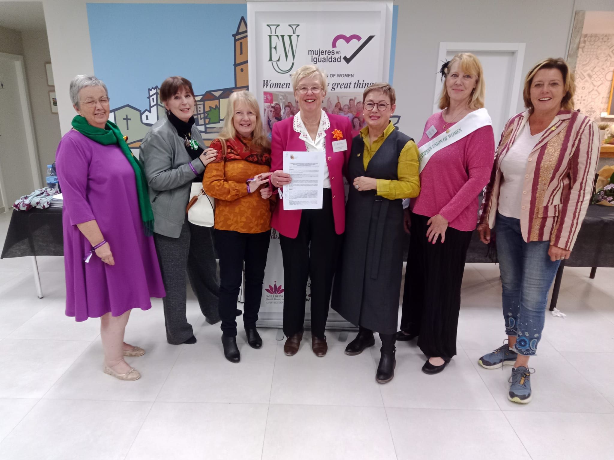 Seven women of the association in front of the EUW and Mujeres en Igualdad banner, one holding a signed document